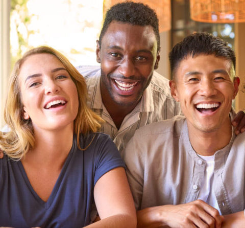 Portrait Of Multi-Racial Friends Sitting Around Table At Home Together Smiling At Camera